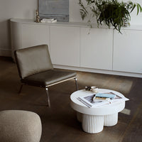 Modern gray chair and round white coffee table with textured base, set against earthy wood tones and soft neutrals.