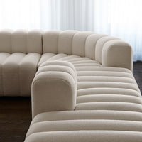 Beige curved sectional sofa with vertical tufted pattern in a modern design. Soft texture and elegant look for any space.