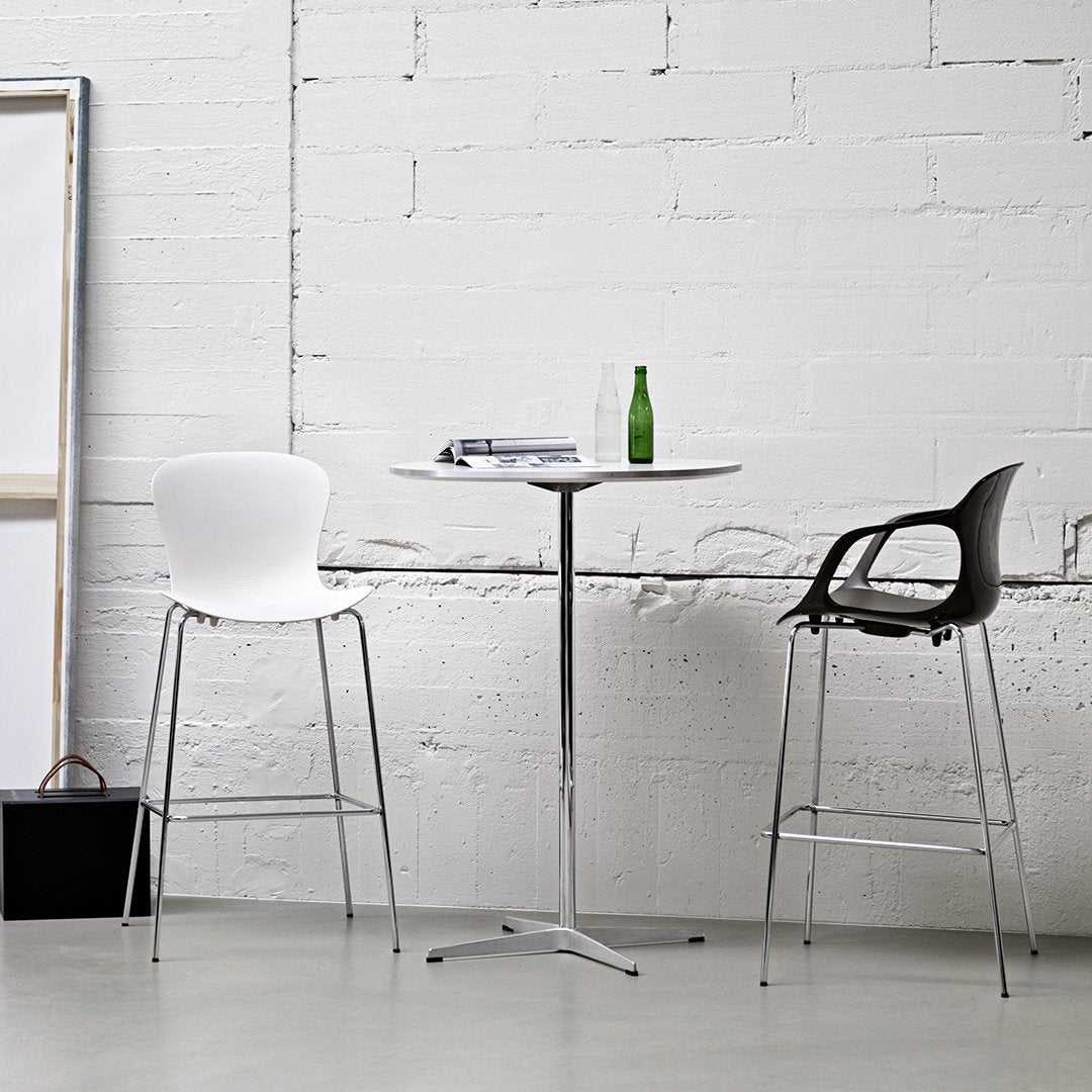 Modern bar table with a sleek white top and silver base, paired with chic black and white chairs against a minimalist backdrop.