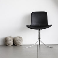 Black modern chair with a sleek design, complemented by two beige yarn balls in a minimalist setting.