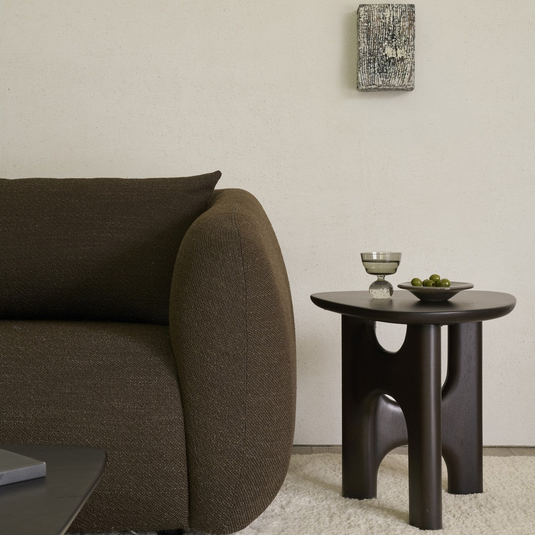 Brown textured sofa with a curved armrest beside a sleek dark wood side table, creating a modern minimalist look.