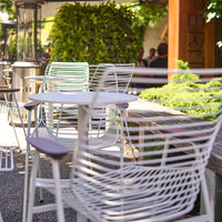 "Modern outdoor seating with white wire chairs and natural wooden accents against a lush green backdrop."