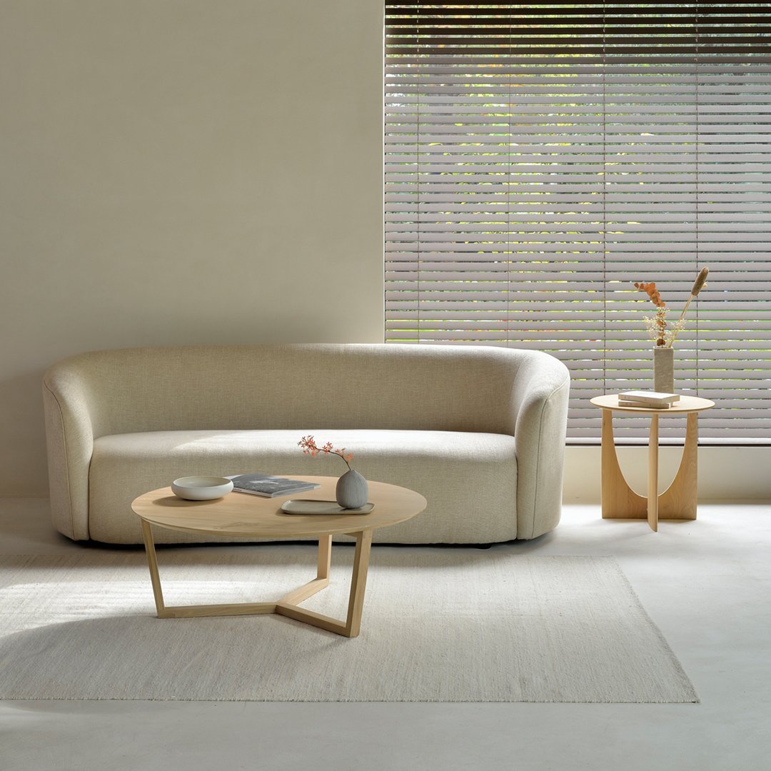 Soft beige curved sofa with a minimalist design, paired with a light wooden coffee table and neutral-toned rug.