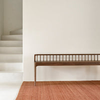 "Rustic brown bench on a textured orange rug, set against a neutral white wall and minimalist staircase."