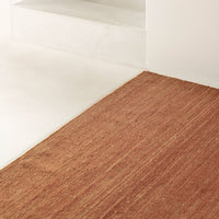 Textured rug in warm rust color with subtle striped pattern, perfect for adding warmth to any space.
