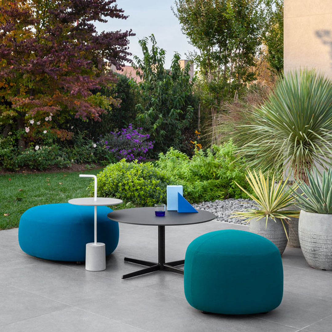 Teal poufs and a sleek black table contrast with the lush green garden and vibrant purple flowers.