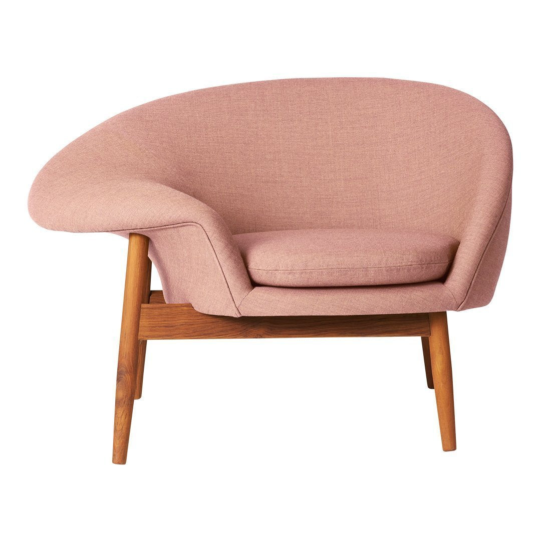 Light pink upholstered chair with a smooth, rounded silhouette and wooden legs. Cozy, modern design accent piece.