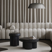 "Soft beige upholstered sofa with textured pattern, paired with black circular side tables and a light gray round rug."