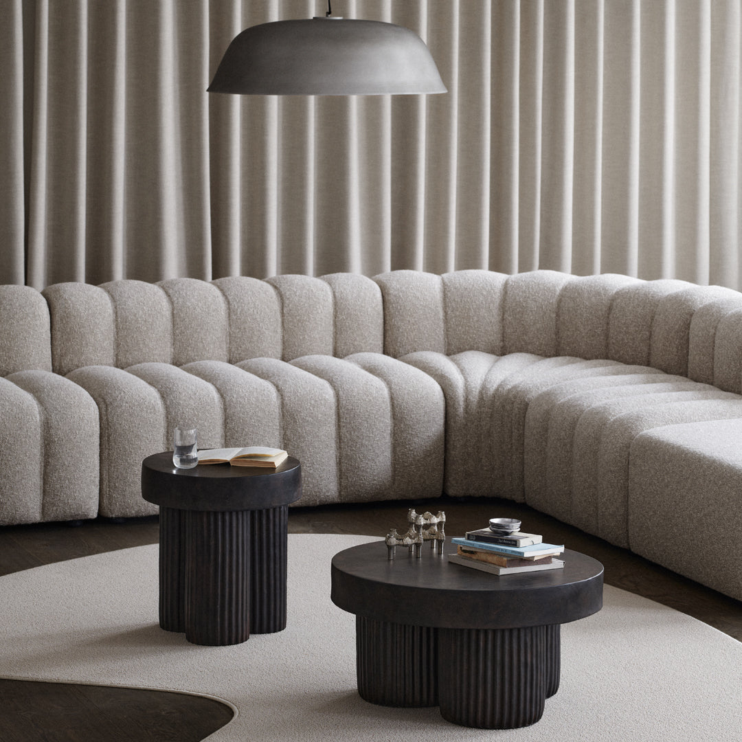 Beige curved sectional sofa with textured upholstery and black ribbed side tables, enhancing modern minimalist decor.