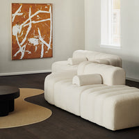 Cream-colored contemporary sofa with organic curves, paired with an abstract orange and white art piece on the wall.