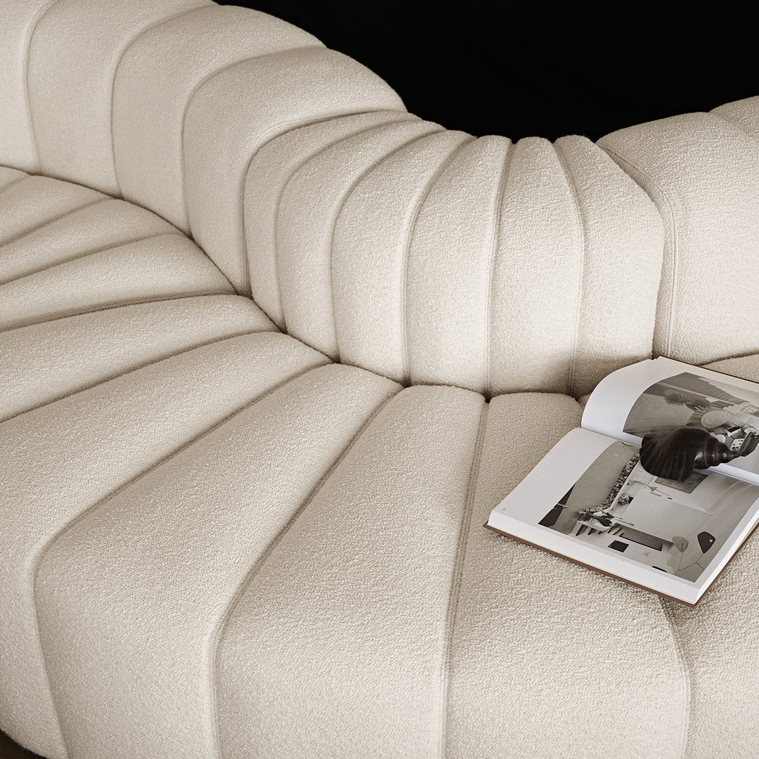 Beige curved sofa with soft, textured fabric showcasing elegant pleats and a modern design.