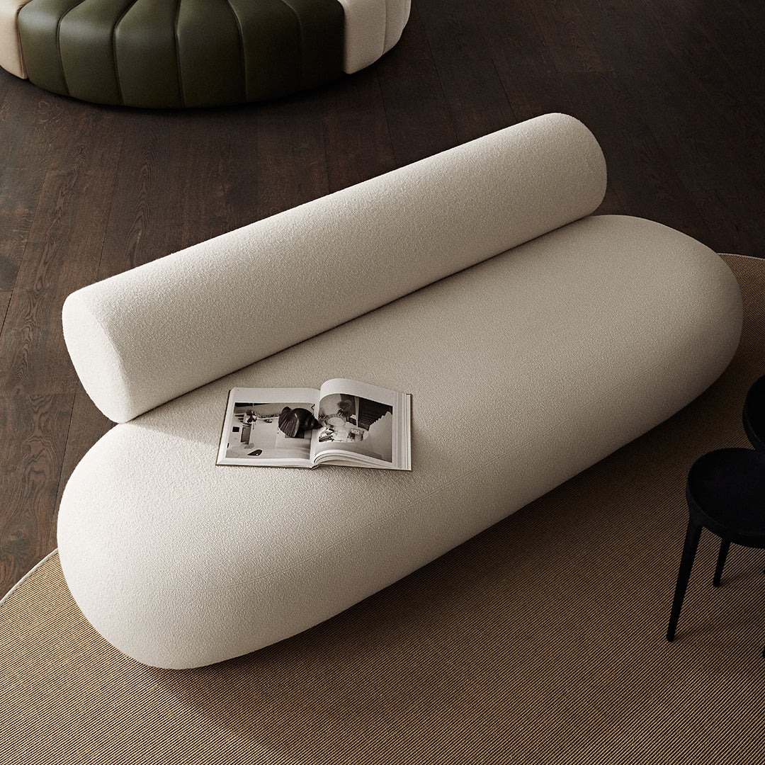 Beige curved sofa with a cylindrical cushion, minimalist design, soft texture, complemented by neutral-toned surroundings.