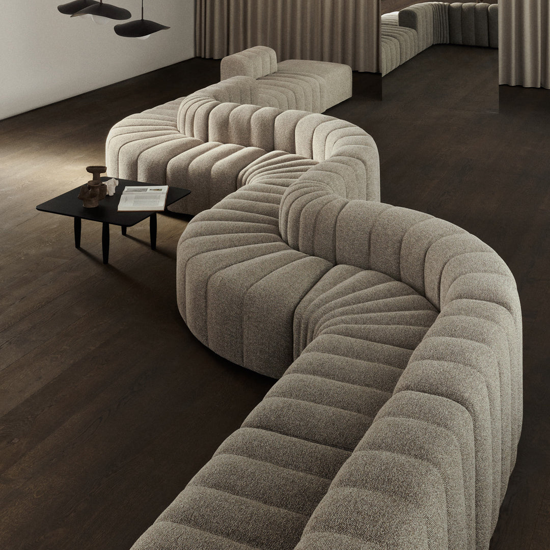 Curved beige sofa with a textured, wavy pattern in a modern interior setting. Dark wooden floor enhances elegance.
