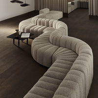 Curved beige sofa with a textured, wavy pattern in a modern interior setting. Dark wooden floor enhances elegance.