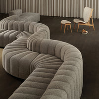 Curved gray sectional sofa with textured, ribbed patterns on a dark wood floor, complemented by light wooden chairs.