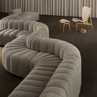 Curved gray sofa with tufted texture, paired with minimalist wooden chairs in a modern interior setting.