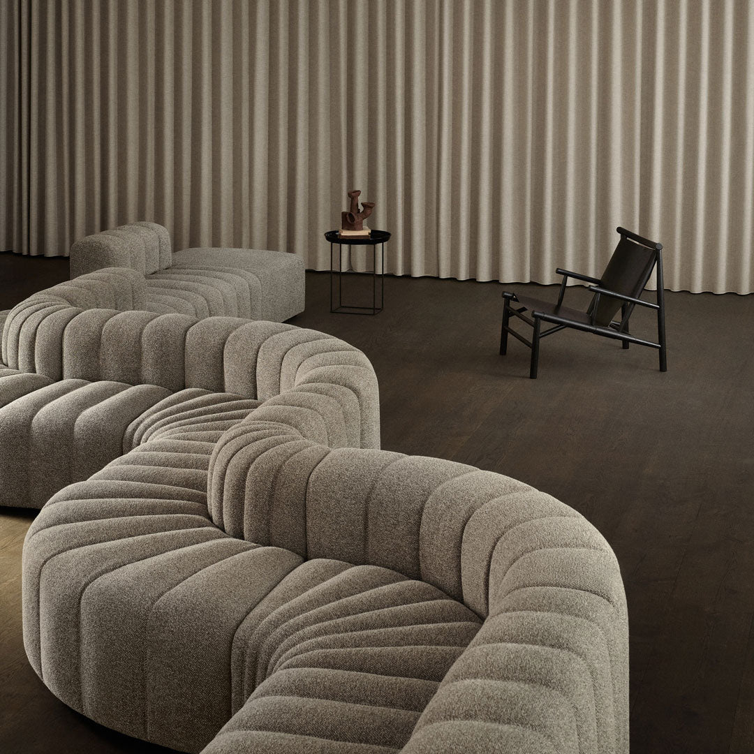 Textured beige curved sofa with subtle vertical and horizontal patterns, set against a muted, neutral backdrop.