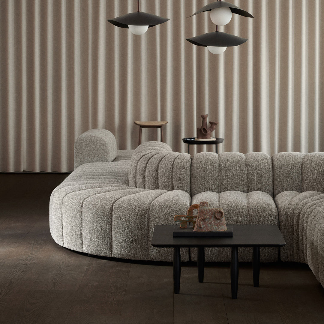 Curved beige sofa with textured upholstery, paired with black accents and soft, neutral-toned decor elements.