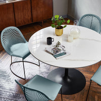 Round white marble table with black base, complemented by teal mesh chairs in a modern, stylish setting.