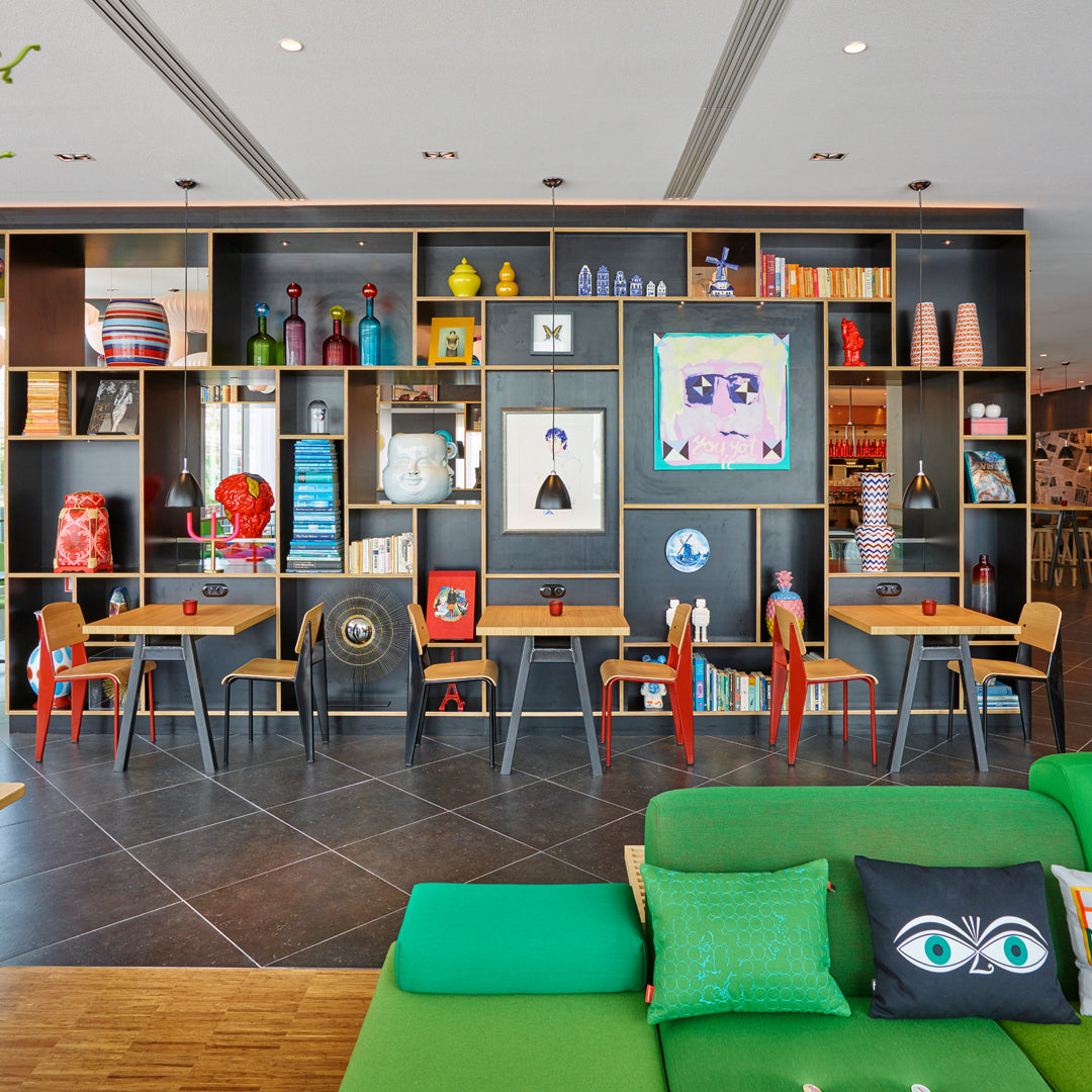 Bright green sofa with colorful pillows, multi-colored decor on black shelves, and wooden tables in a vibrant interior setting.