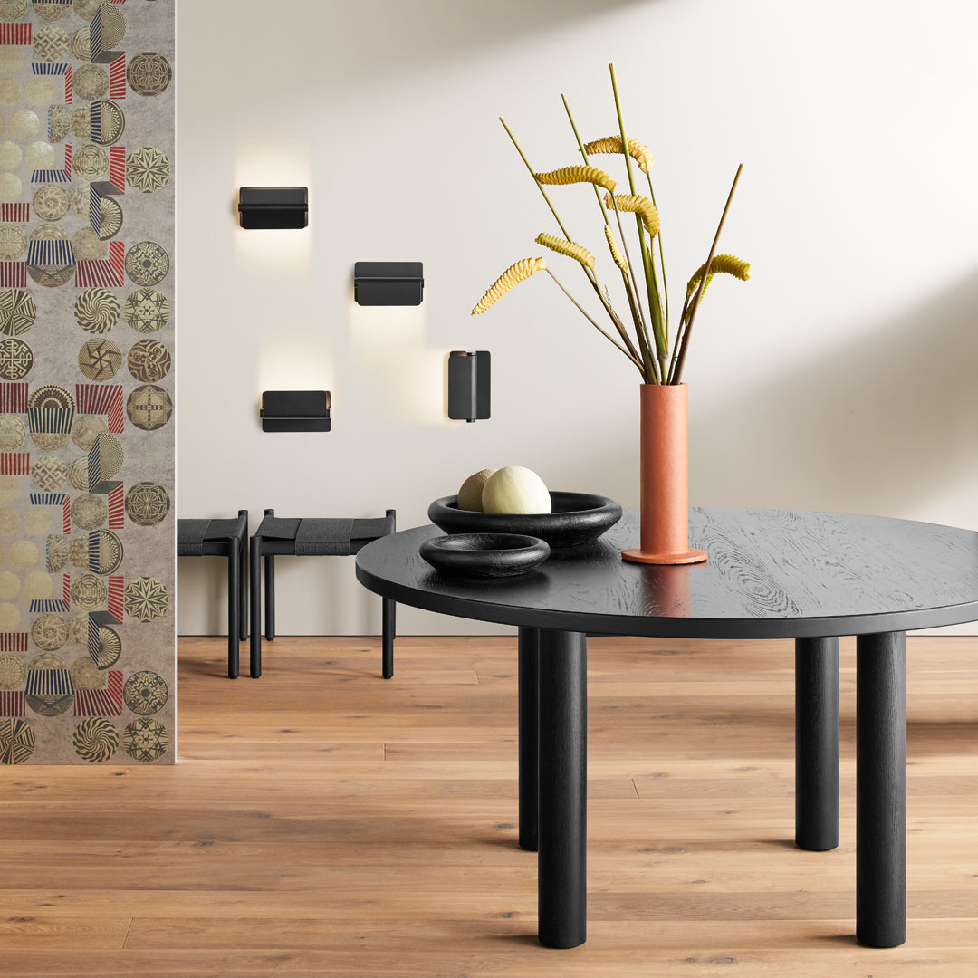 Black round table with textured top, black bowls, and an orange vase, set against a colorful patterned wall.