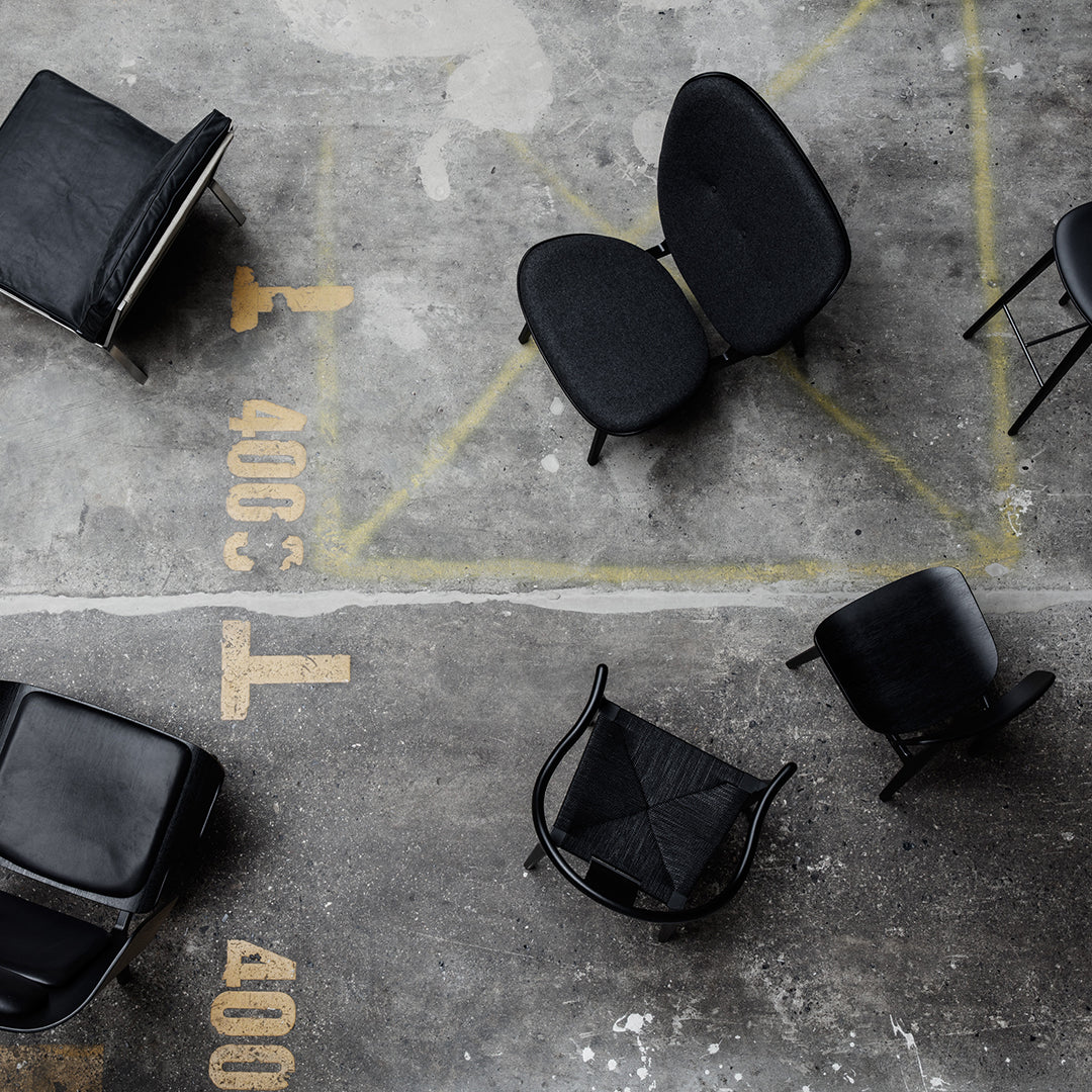 Black chairs in various patterns on a textured concrete floor with yellow markings. Modern minimalist design elements.