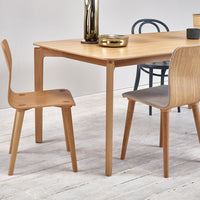 Natural wood dining table with light oak finish, paired with gray and black chairs on a whitewashed wooden floor.