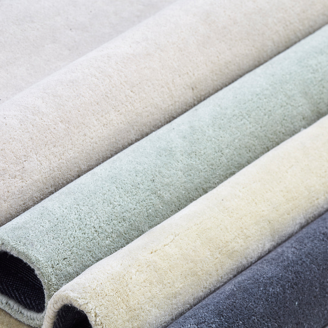 Neutral-colored rugs in shades of beige, soft green, light yellow, and dark gray, showcasing subtle textures.