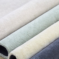 Neutral-colored rugs in shades of beige, soft green, light yellow, and dark gray, showcasing subtle textures.
