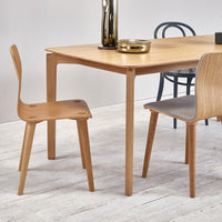 Light wood dining table with natural finish, paired with simple beige and gray chairs in a minimalist setting.
