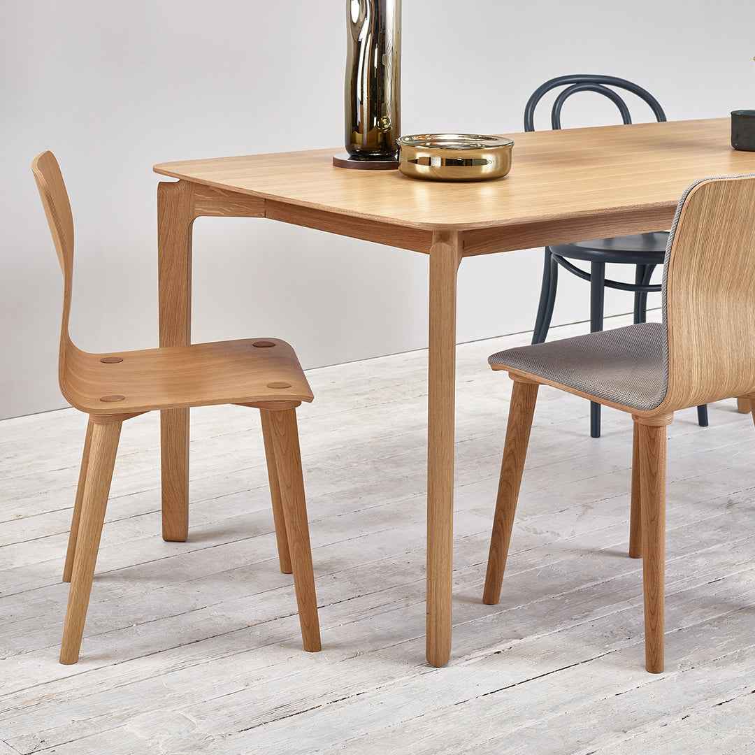 Natural wood dining table with light oak finish, paired with light gray and dark blue chair accents on a white wood floor.