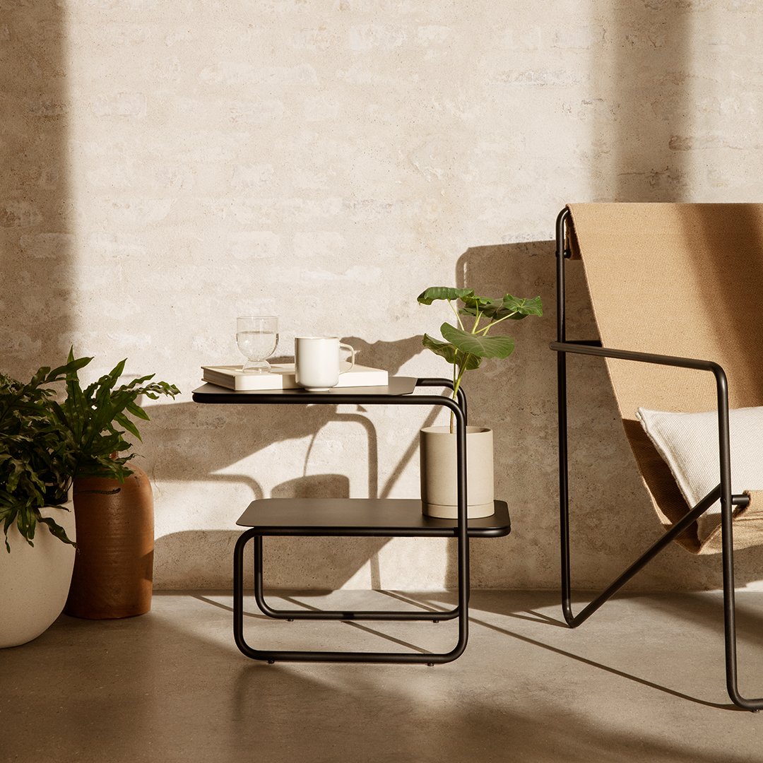 Stylish black metal side table with a sleek design, accented by earthy tones and greenery in a modern setting.
