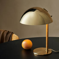 Gold dome lamp with a sleek design, complemented by an orange fruit on a dark table. Stylish and modern aesthetic.