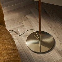 "Gold floor lamp base with a wooden pole on light herringbone wood flooring, complements a textured mustard yellow couch."