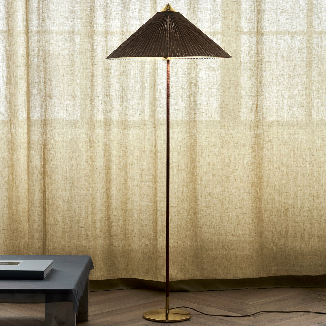Dark brown pleated lamp shade with gold base, set against a soft beige curtain backdrop.