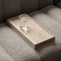 Light beige wooden tray with smooth surface, paired with a clear glass of water on textured gray sofa fabric.