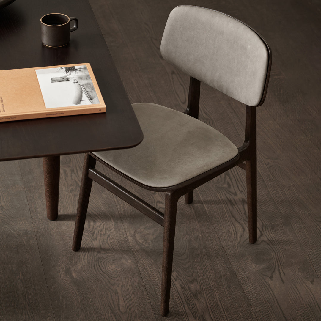 Gray upholstered chair with a smooth surface and dark wooden legs, set against a dark wood floor. Modern and minimalist design.
