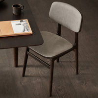 Gray upholstered chair with a smooth surface and dark wooden legs, set against a dark wood floor. Modern and minimalist design.