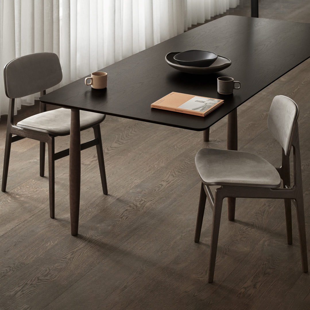 "Modern dining table with a sleek black top, paired with gray velvet chairs on warm wood flooring."