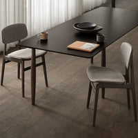 "Modern dining table with a sleek black top, paired with gray velvet chairs on warm wood flooring."