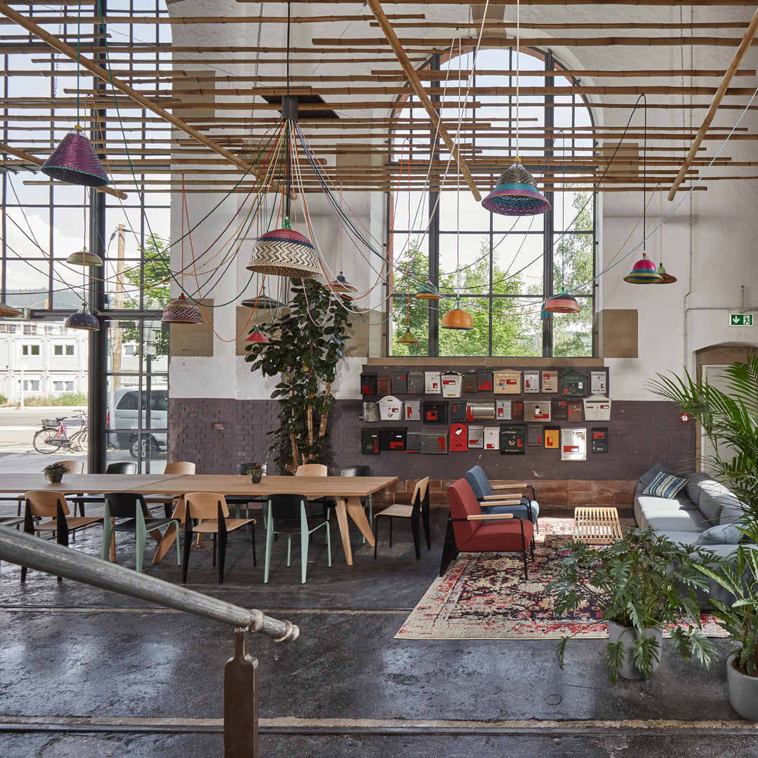 Modern interior with vibrant hanging lamps, greenery, wood furniture, and a patterned area rug on a dark floor.