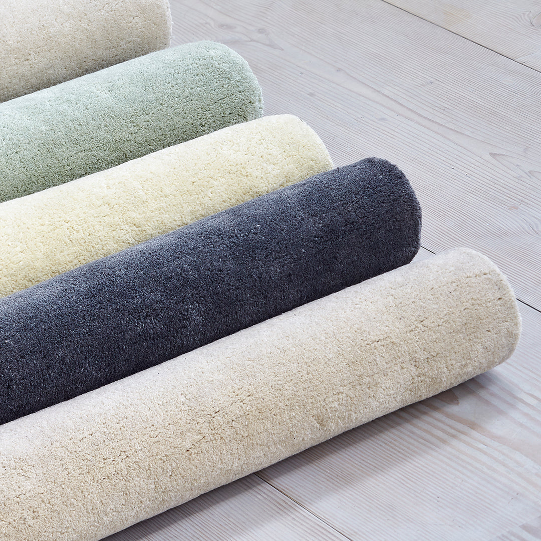 Soft, plush bath rugs in light green, pale yellow, dark gray, and creamy beige, showcasing a gradient of soothing colors.