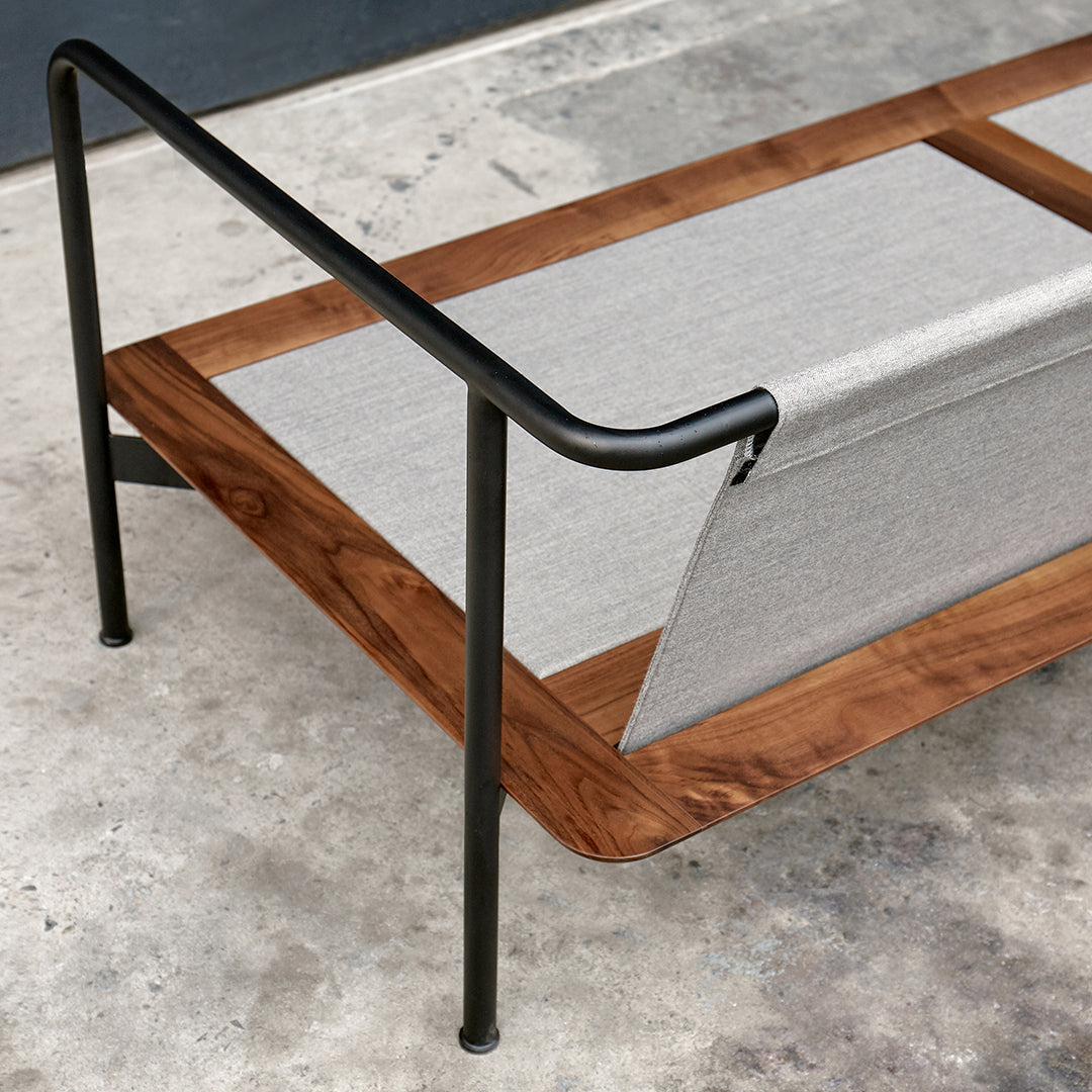 Modern lounge chair with a natural wood finish, grey fabric, and sleek black metal accents on a concrete background.