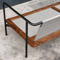 Modern lounge chair with a natural wood finish, grey fabric, and sleek black metal accents on a concrete background.