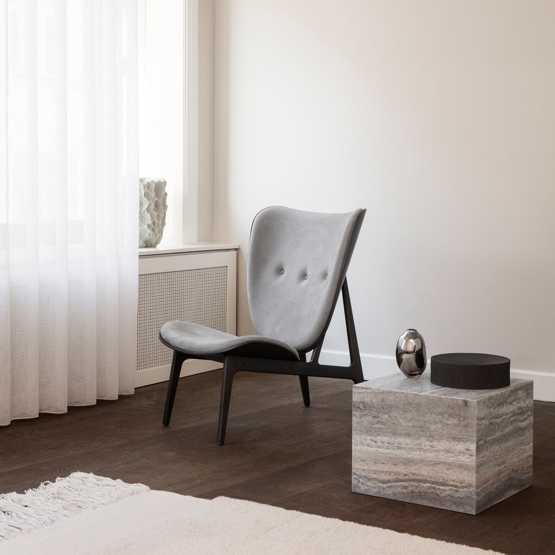 Gray upholstered chair with black legs next to a textured marble table in a neutral-toned room. Cozy design vibes.