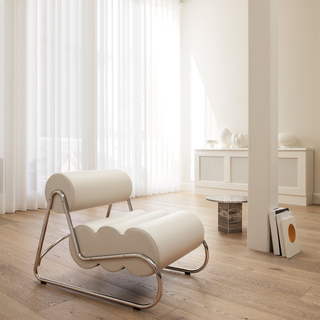 Modern white lounge chair with a unique scalloped design and sleek chrome frame, set in a bright, airy room.