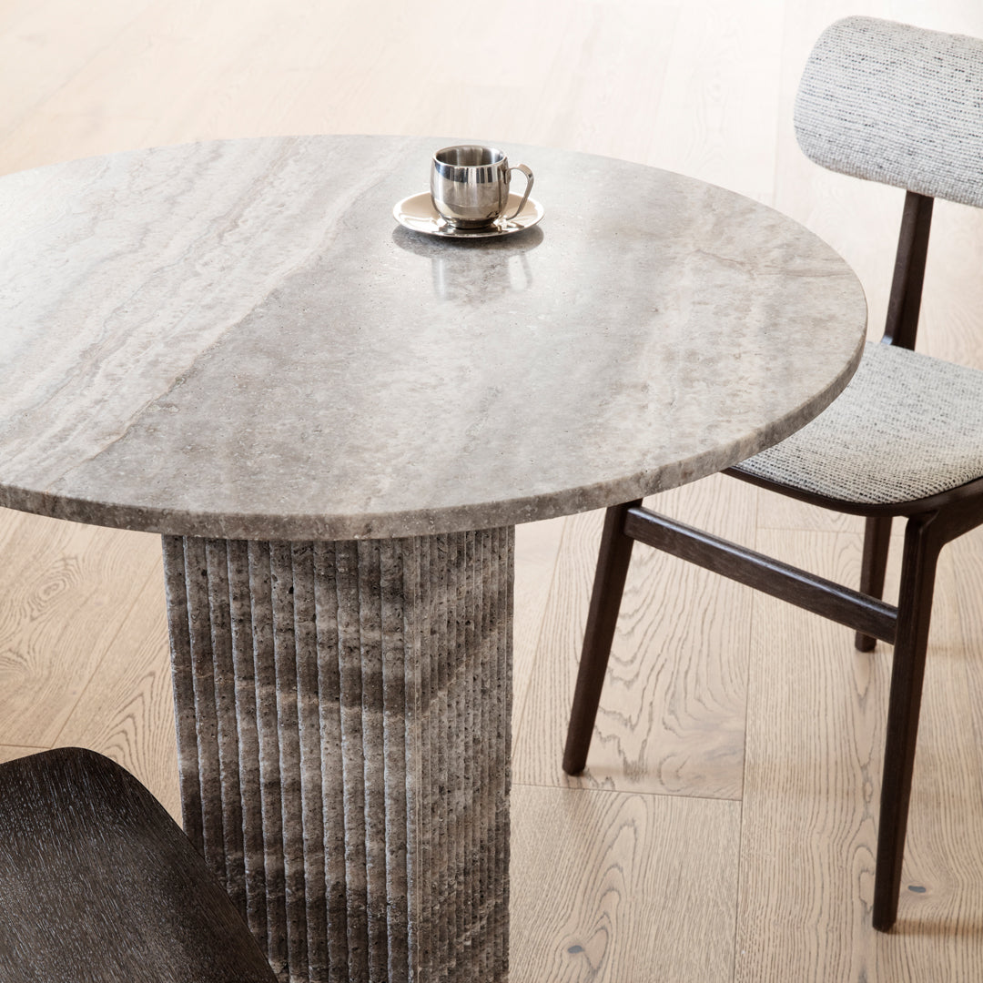Gray stone round table with vertical ribbed pedestal and light gray patterned chair on oak flooring.