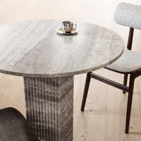 Gray stone round table with vertical ribbed pedestal and light gray patterned chair on oak flooring.