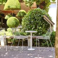 "Stylish white outdoor chairs with sleek lines, set against lush green foliage and geometric topiary shapes."