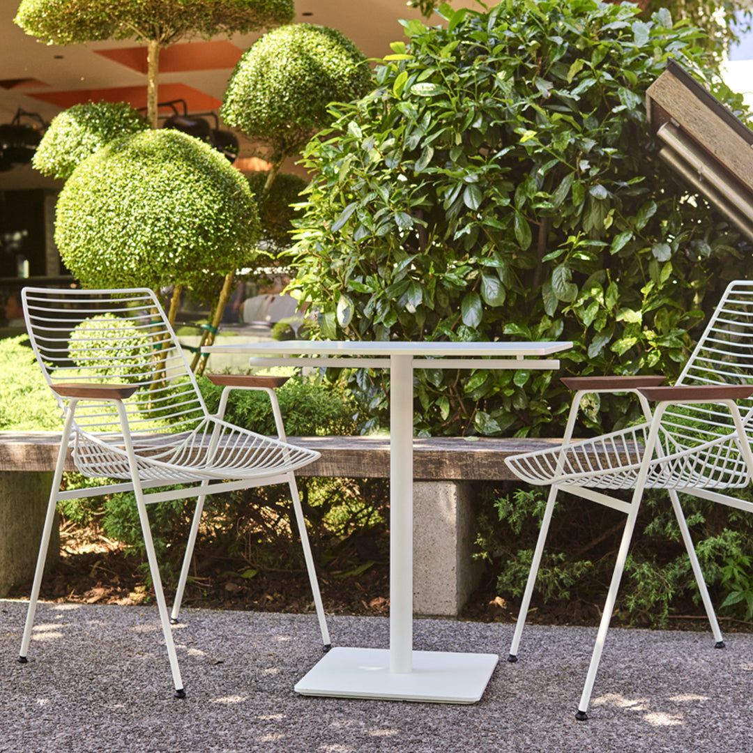 "White metal outdoor table with striped chairs amid lush greenery and neatly trimmed hedges."